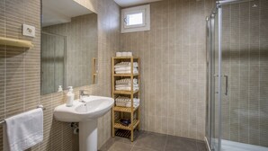 A bathroom with a sink, mirror, towel rack, shelf with towels, and a shower area. - Apartamento Exterior Superior de 2 Dormitorios 1 Baño (Malasaña)