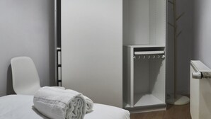 A hotel room with a bed, a white chair, a shower area, and a coat rack. - Apartamento Bajo Interior 2 Dorm, 3 Camas (Madrid)