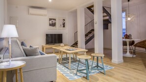 A modern living room with a sofa, coffee table, and a TV. There is a staircase leading to another level. - Apartamento Interior Duplex 2 Dormitorios 2 Baños (Malasaña)