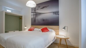 A modern bedroom with a large bed, a headboard, a bedside table, a lamp, and a wall art of a bridge. - Apartamento Interior Duplex 2 Dormitorios 2 Baños (Malasaña)