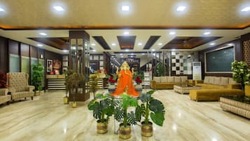 A hotel lobby with a reception desk, seating area, and decorative plants.