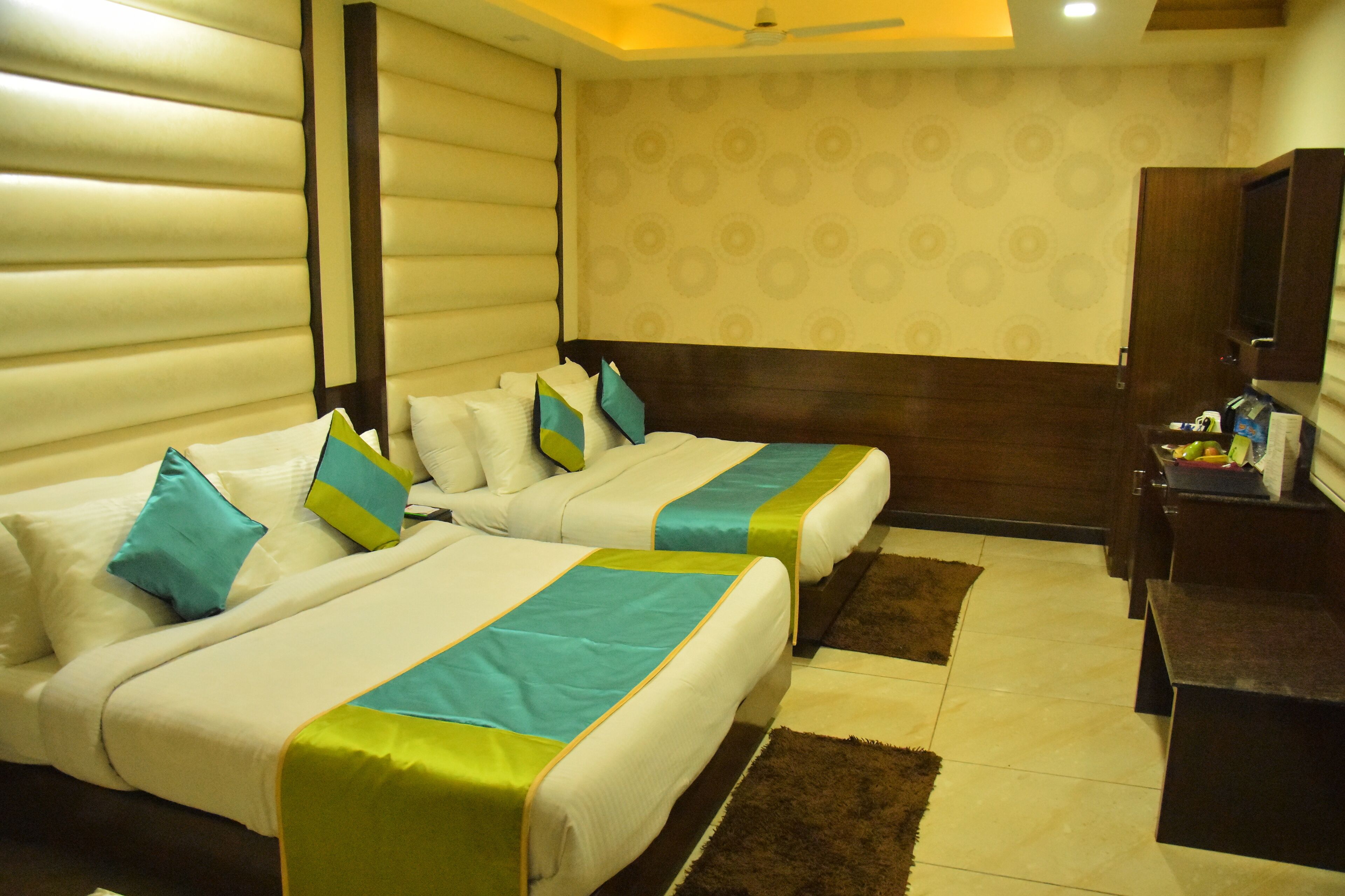A hotel room with two beds, a wooden headboard, a ceiling fan, a patterned wall, and a small desk with a mirror.