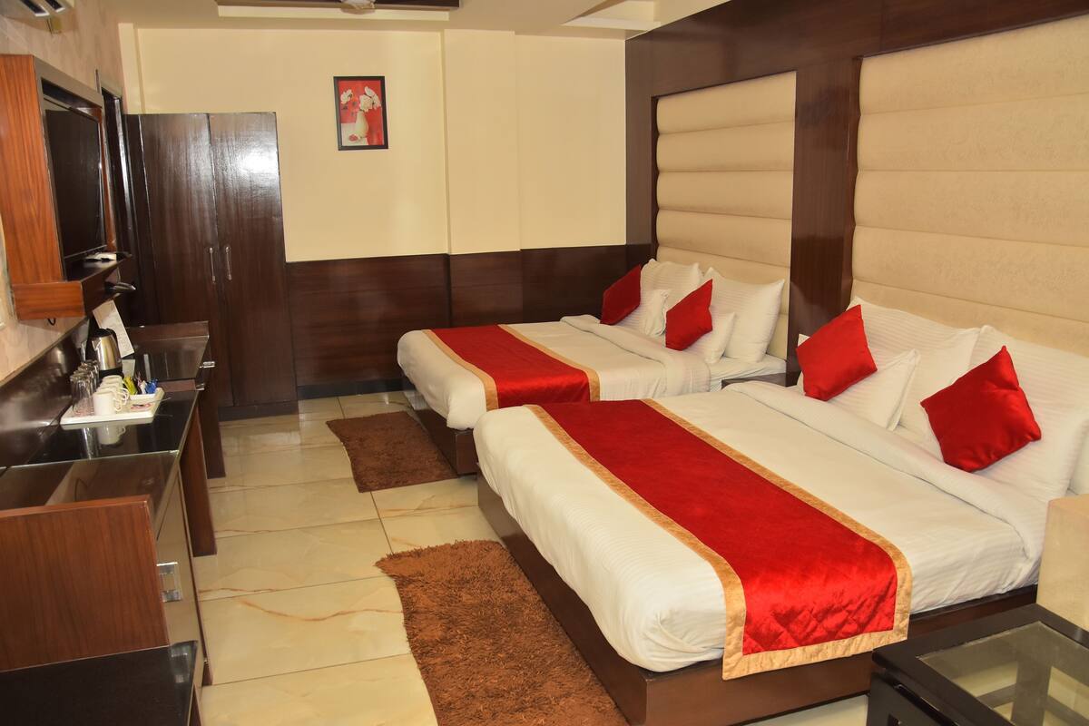 A hotel room with two beds, a TV, a desk with a coffee machine, and a brown rug.