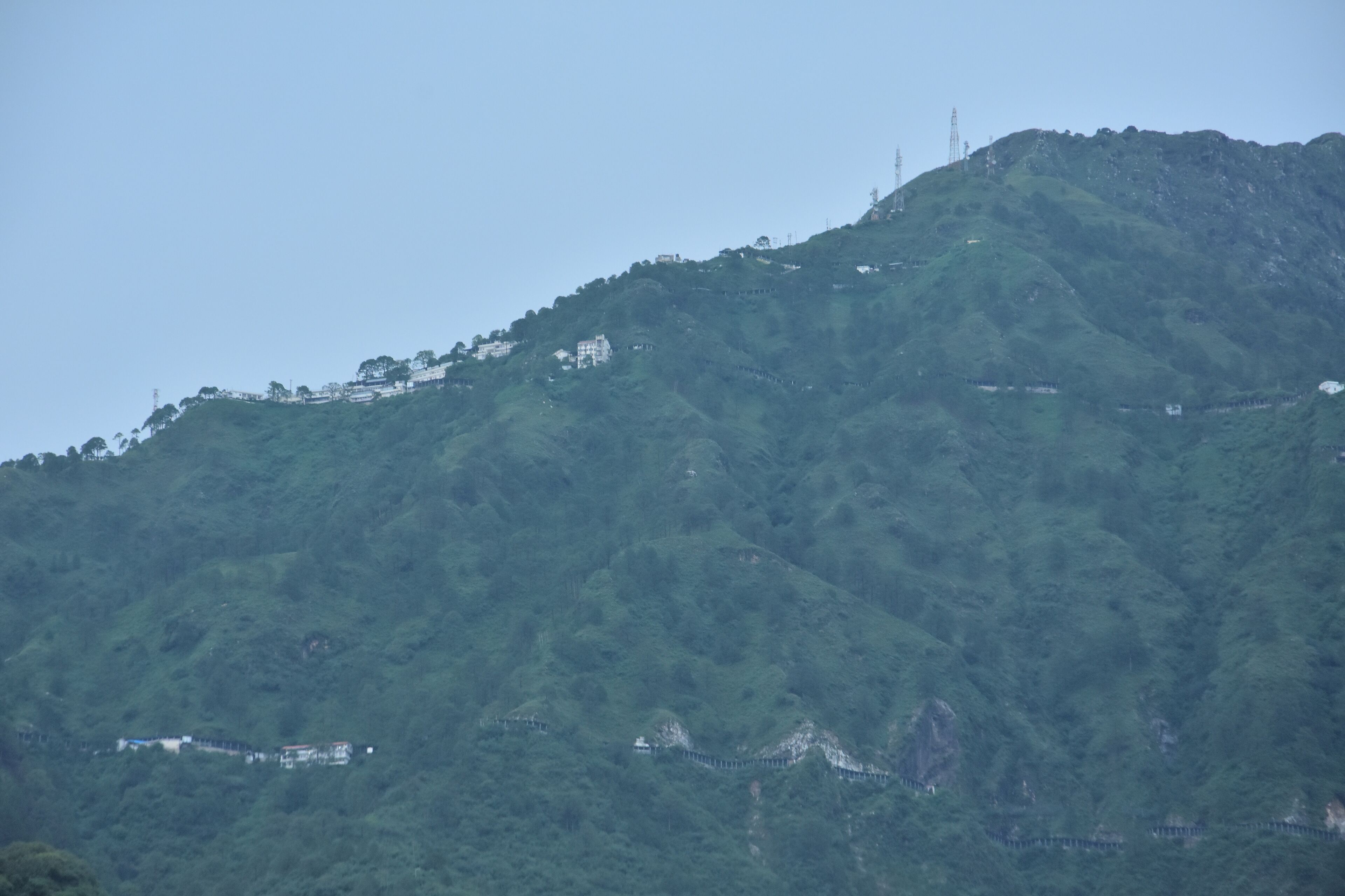 A mountainous landscape with a dense forest and a few buildings on the slopes.