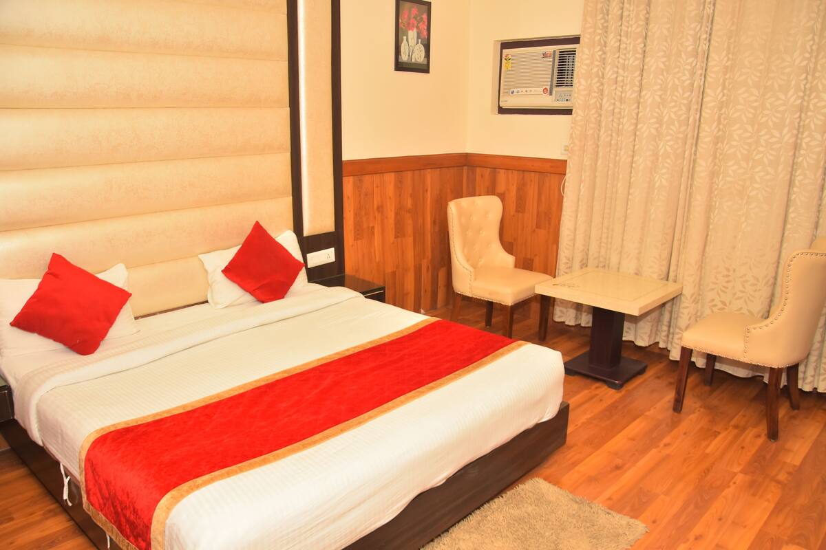 A hotel room with a large bed, two chairs, a small table, and a window with curtains.