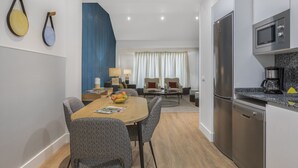 A modern kitchen with a refrigerator, microwave, and coffee maker. There is a dining area with a table and chairs, and a living area with a sofa and a lamp. - Apartamento Duplex 2 Dormitorios con Terraza (Madrid)