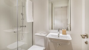 Une salle de bain moderne avec une douche à parois de verre, un lavabo blanc et un miroir au-dessus du lavabo.
