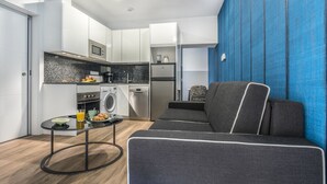 Un espace de vie compact comprenant un coin cuisine, un canapé gris et une petite table ronde sur laquelle sont disposés des aliments pour le petit-déjeuner.