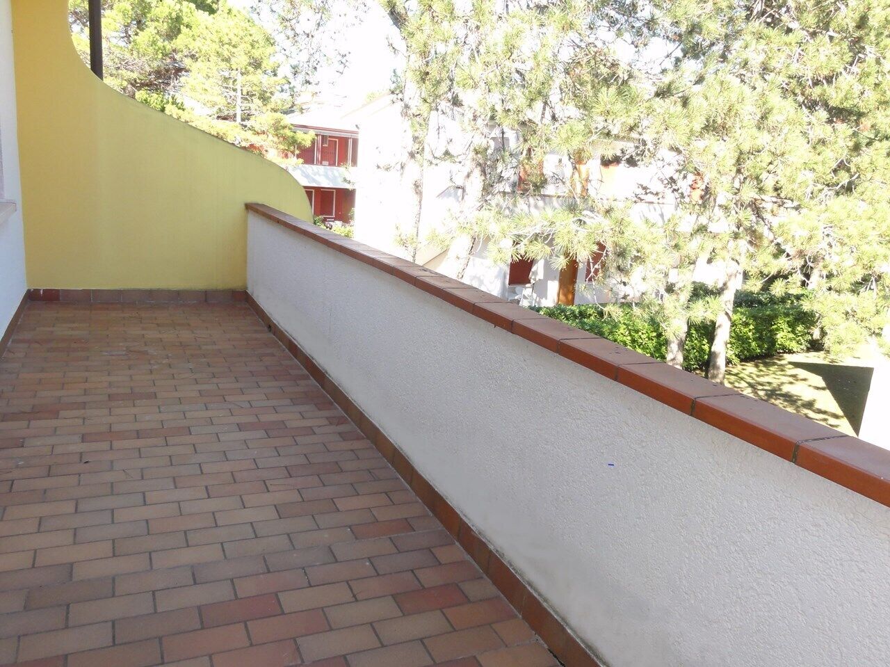 Een balkon met een bakstenen vloer en een witte muur met rode accenten.
