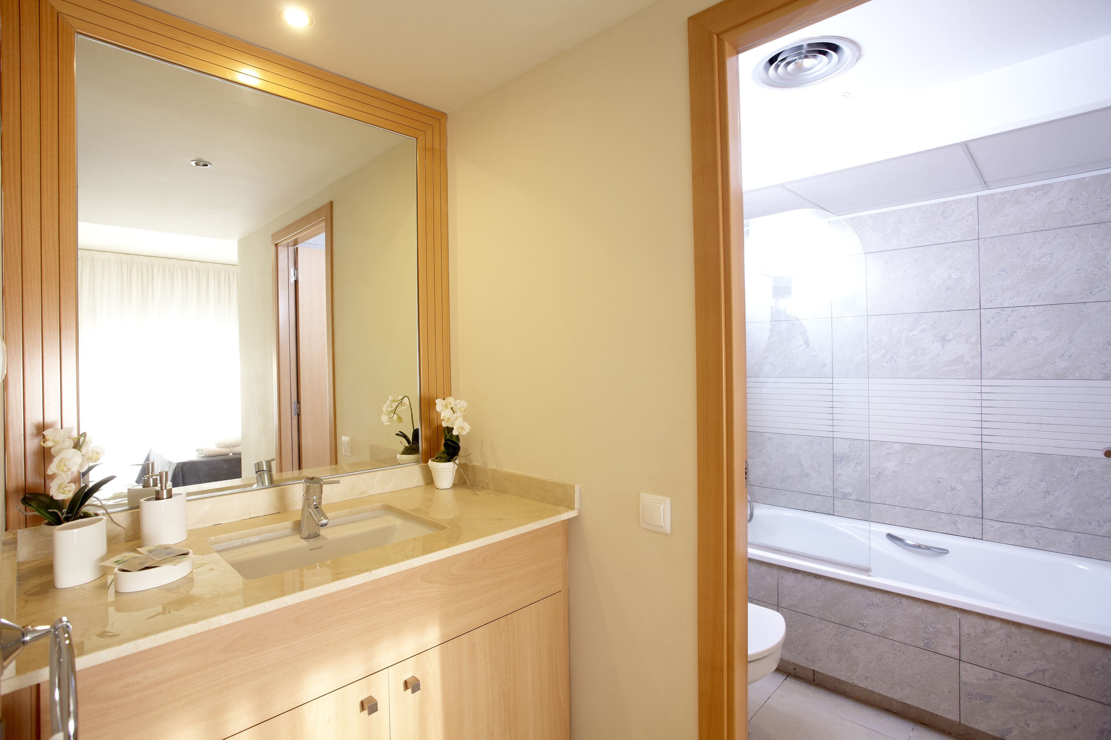 Un baño moderno con tocador de madera, un espejo grande y una bañera.