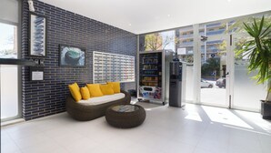 Un hall d’entrée moderne avec un mur en briques, un canapé avec des coussins jaunes, un distributeur automatique et une grande fenêtre donnant sur la rue.