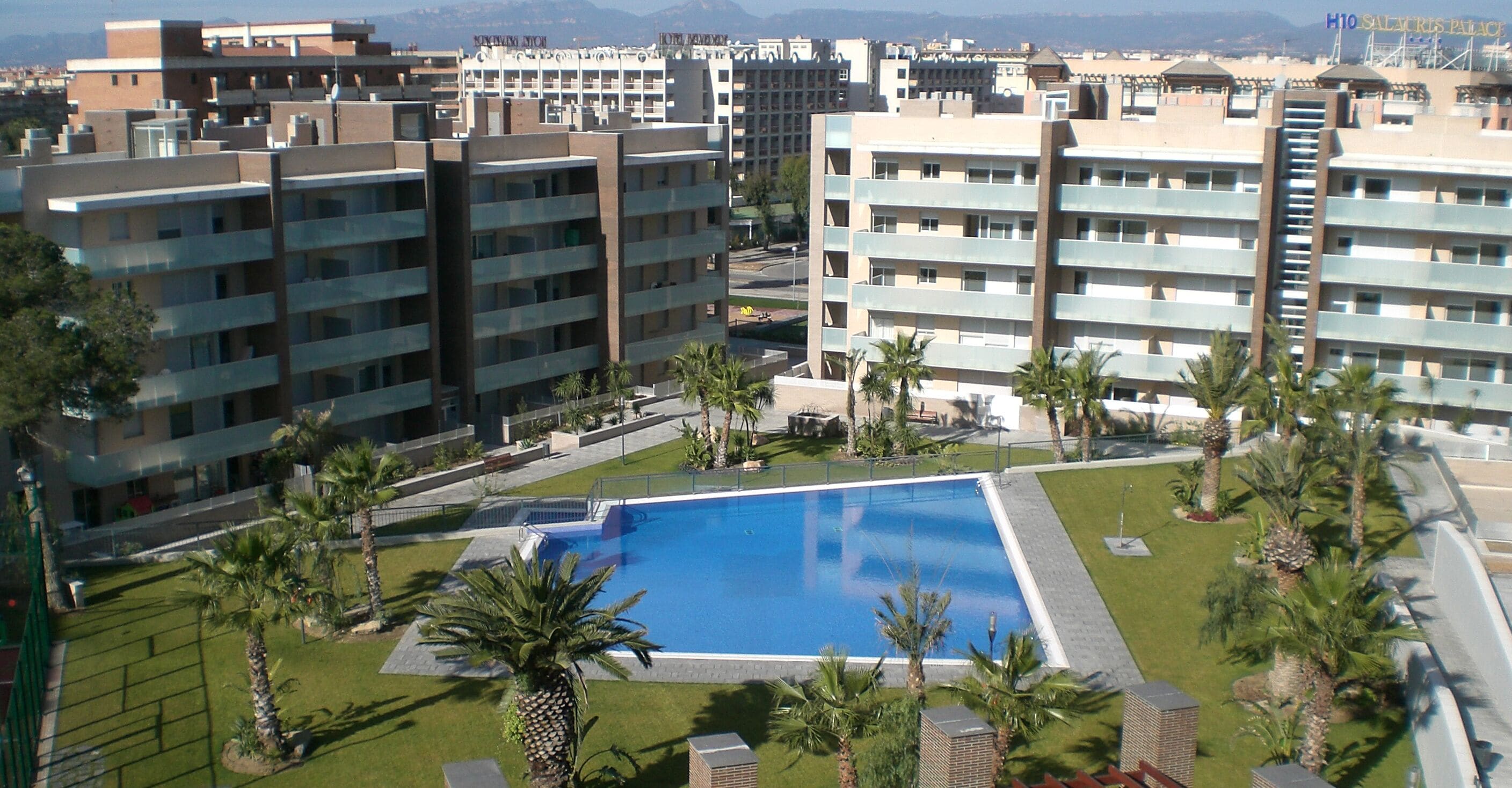 Un hotel con varios pisos, piscina y palmeras.