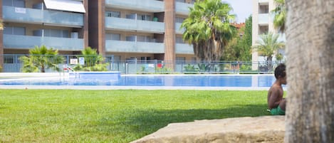 A residential building with multiple balconies, a swimming pool, and palm trees.
