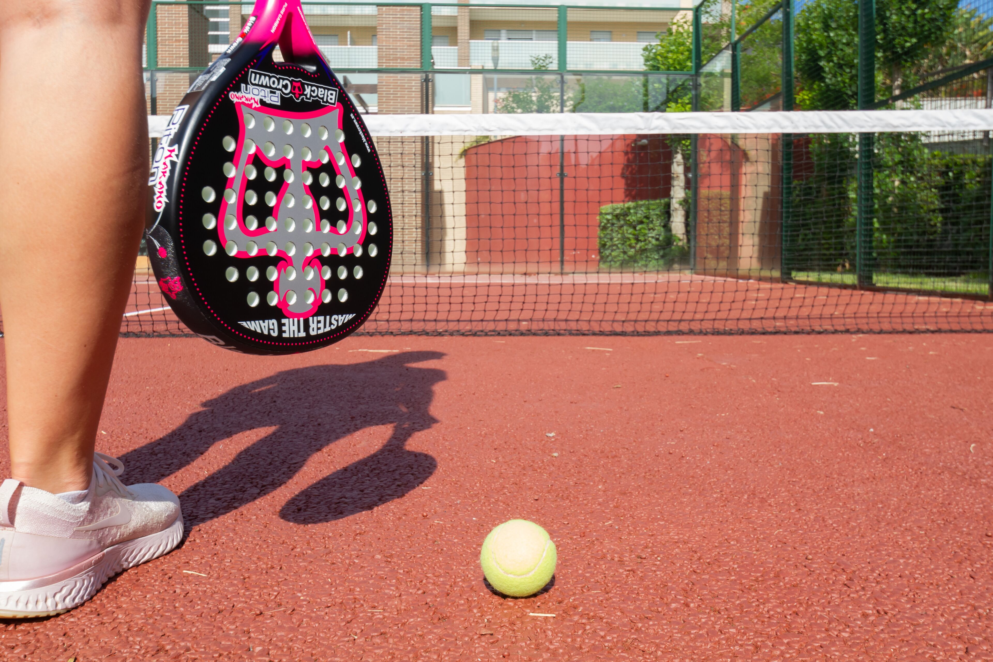 A tennis court with a net, a tennis ball, and a tennis racket.