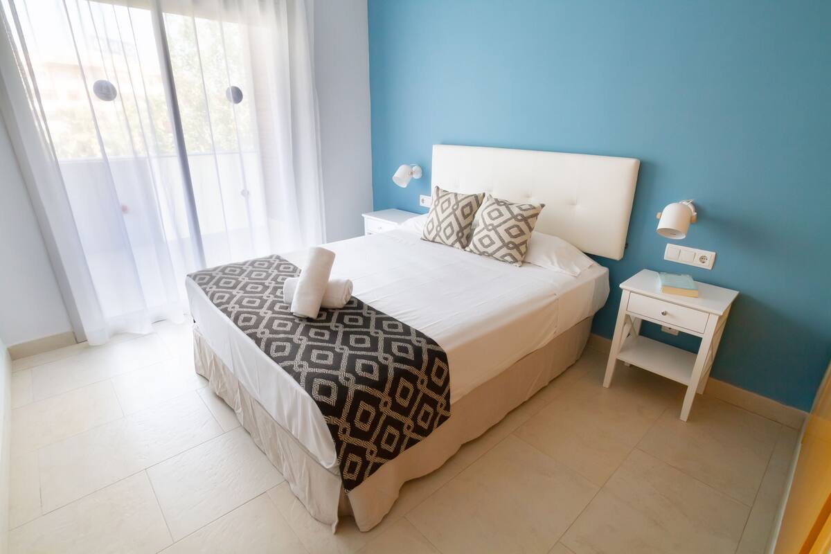 A neatly arranged bedroom with a bed, bedside tables, and a window with curtains.