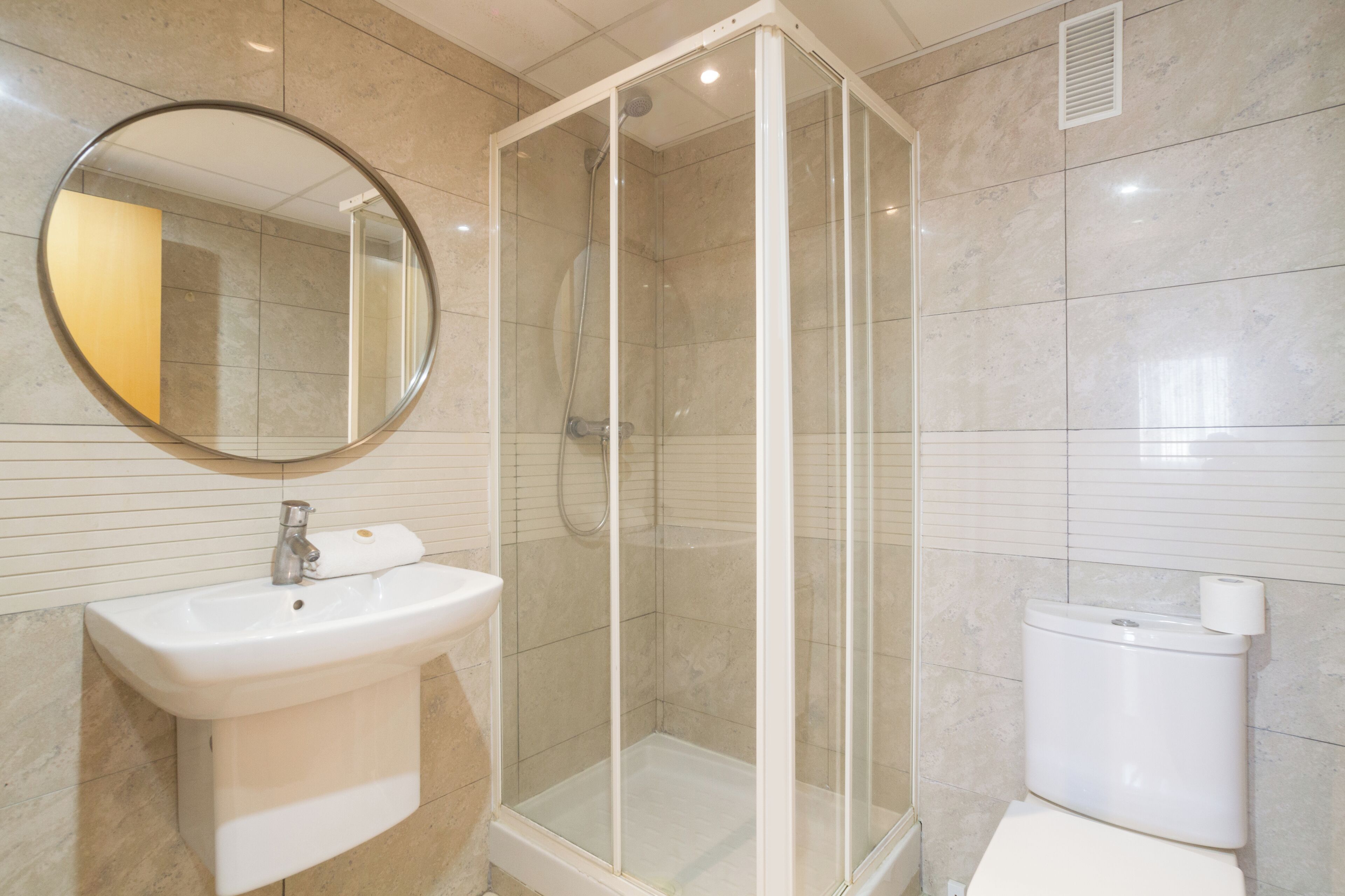 Un baño con ducha envuelta en vidrio, un lavamanos y un inodoro.