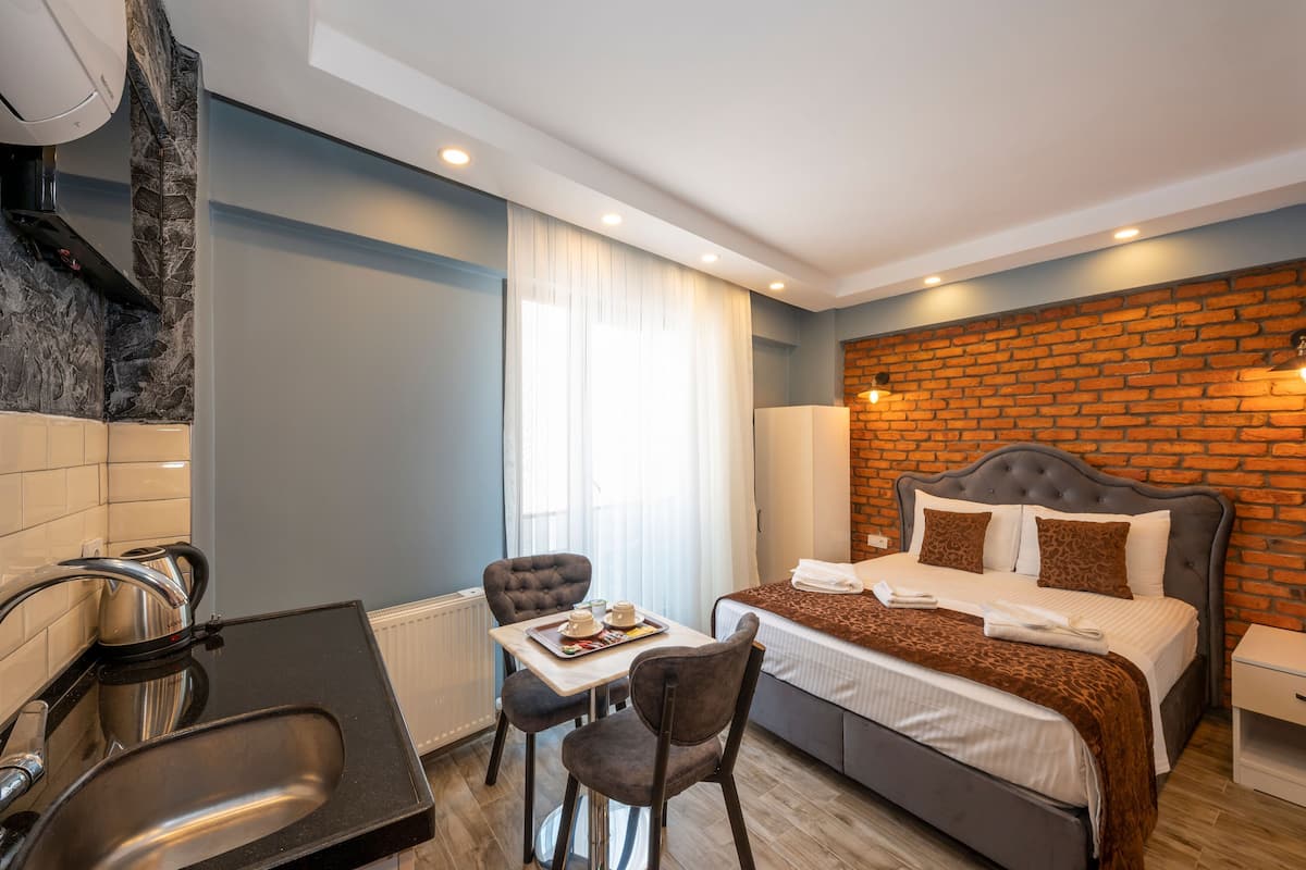 A modern hotel room with a bed, a small table with chairs, a sink, and a brick accent wall.