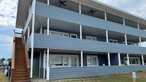 Un edificio de varios pisos con una escalera de madera que conduce a la entrada, un porche cubierto y un letrero que indica estacionamiento privado.