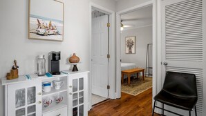 Una habitación con un armario blanco, una cafetera, un florero y un cuadro en la pared.