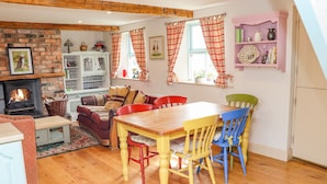 A cozy living room with a fireplace, a dining table with chairs, a sofa, and a bookshelf.