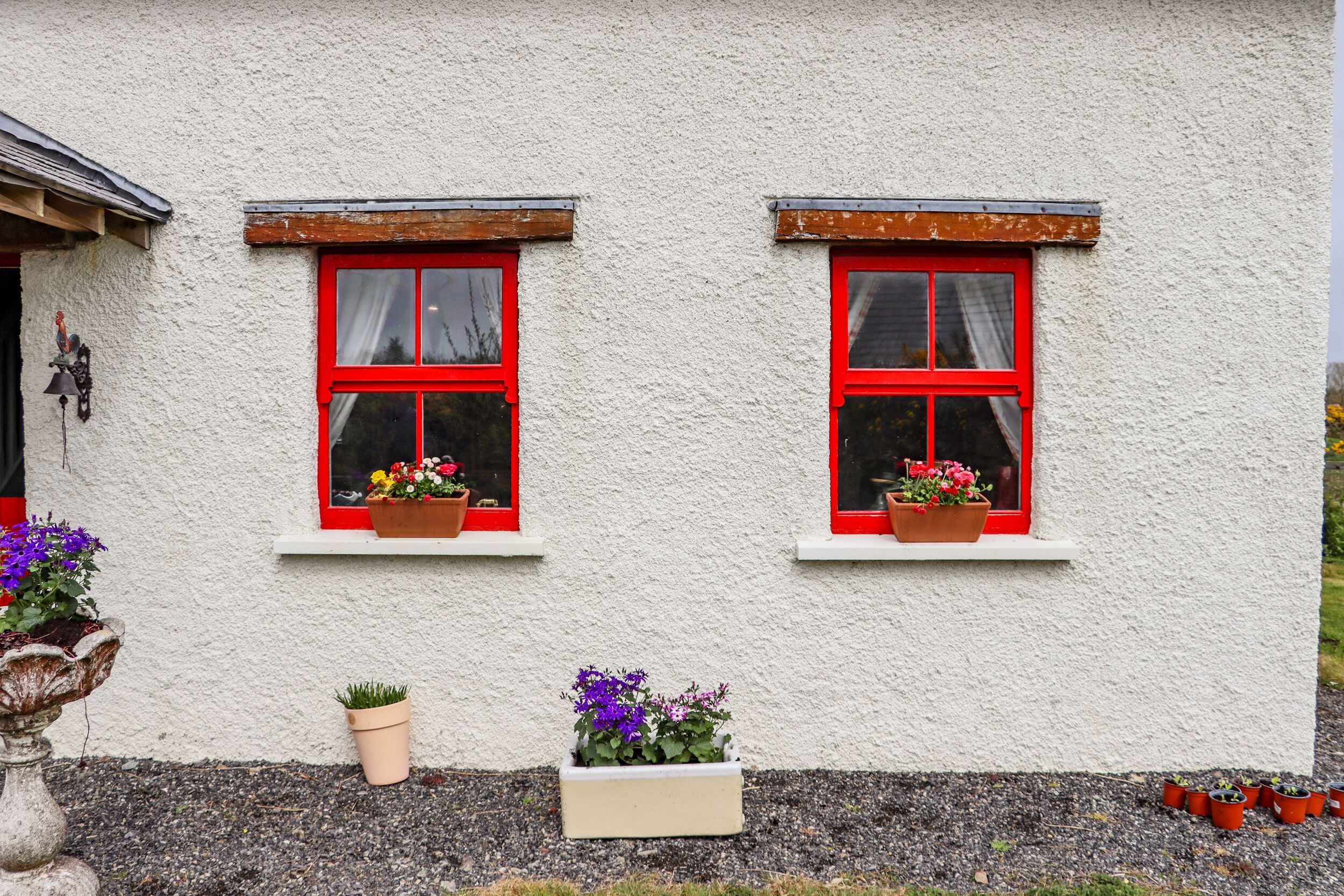 A building with two windows, each with a red frame and potted plants.