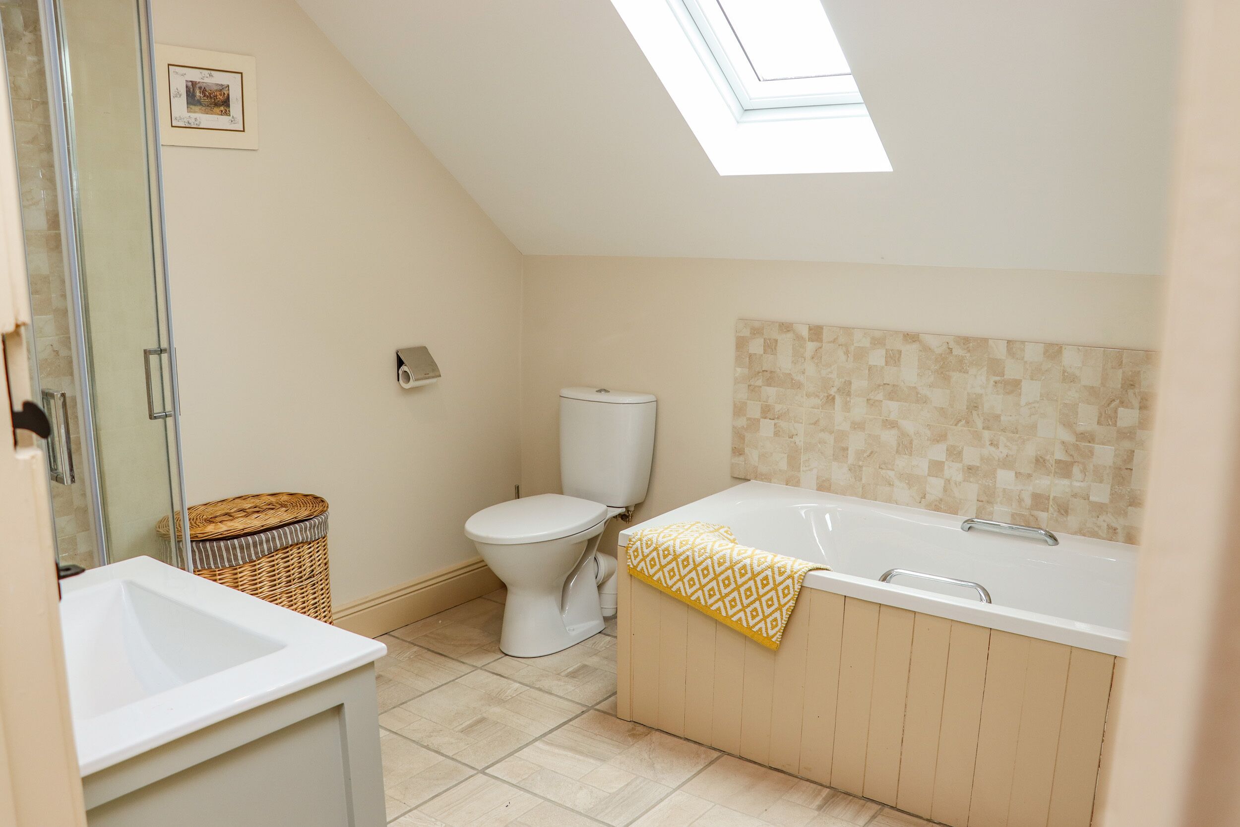 A bathroom with a skylight, a toilet, a bathtub, and a sink.