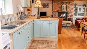 A kitchen with light blue cabinets, a wooden floor, a fireplace, and a dining area with a red chair and table.