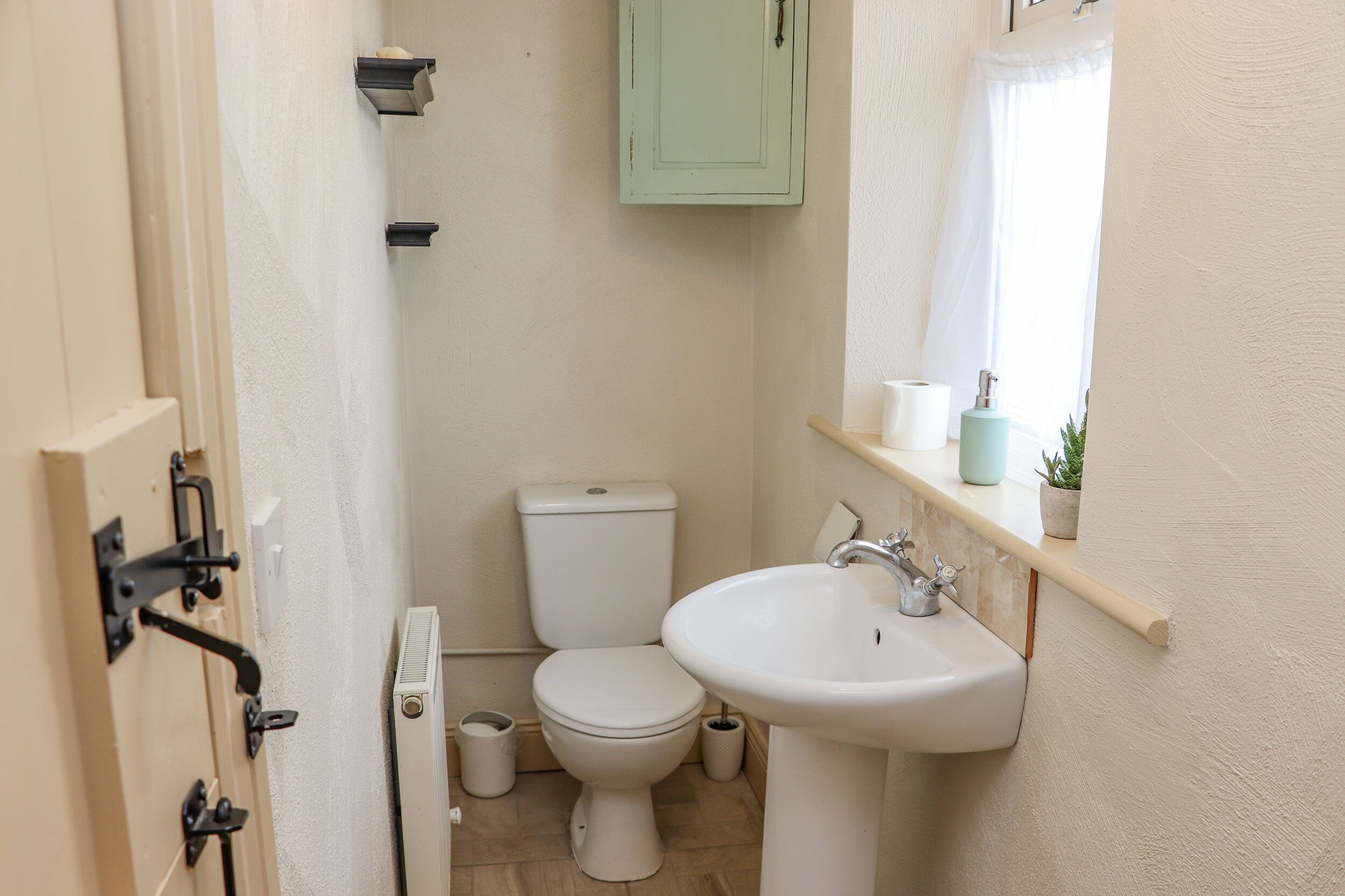 Ein kleines Badezimmer mit Toilette, Waschbecken und einem Fenster mit Vorhang.