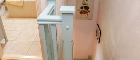 Una escalera con barandilla azul claro que lleva a una habitación con bañera y una obra de arte en la pared con animales.
