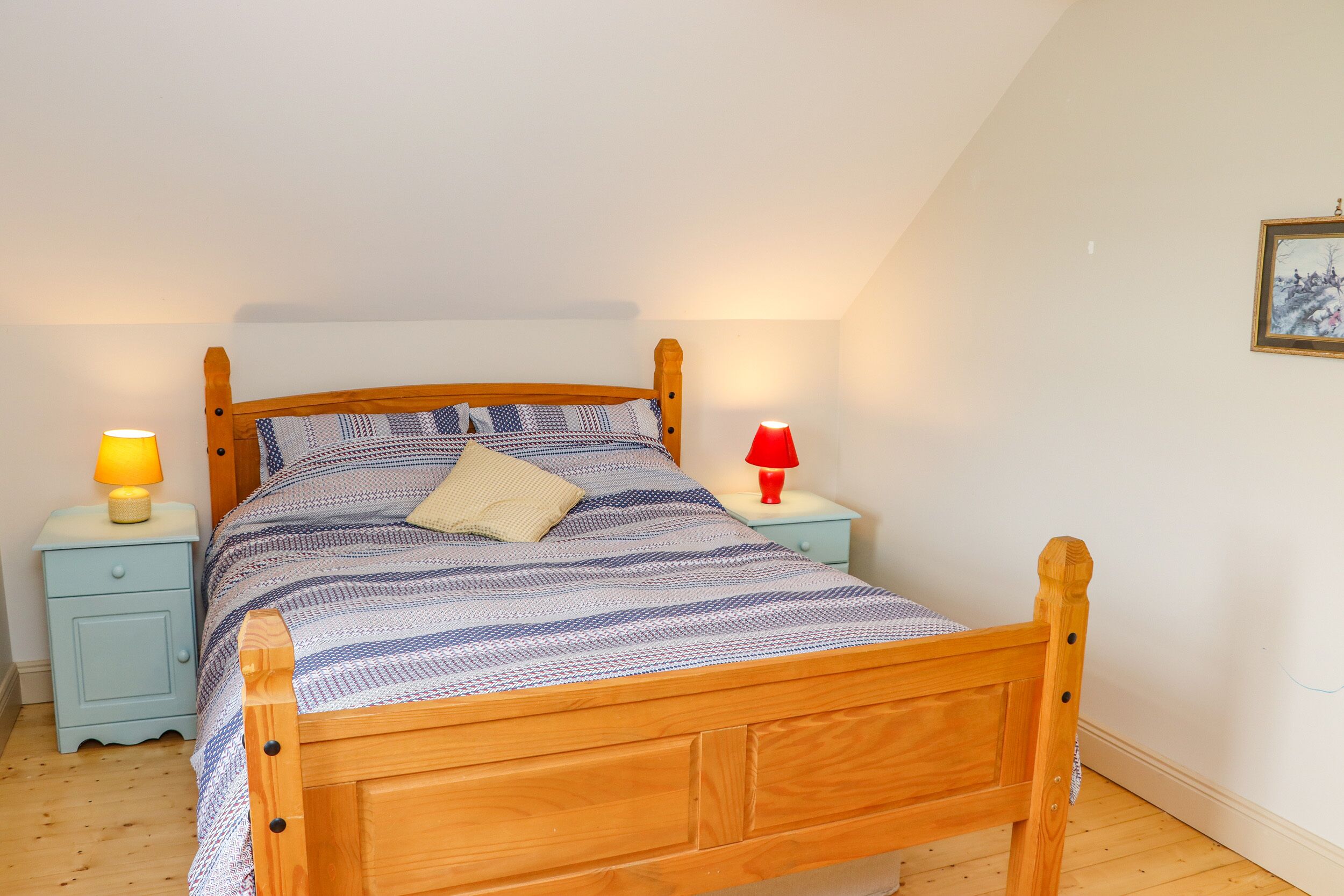 A wooden bed with a striped bedspread and two bedside tables with lamps.
