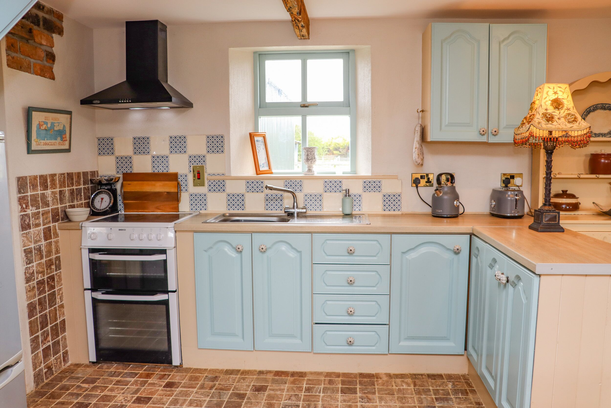 Een keuken met lichtblauwe kastjes, een zwarte afzuigkap, een dubbele oven en een raam boven de spoelbak.
