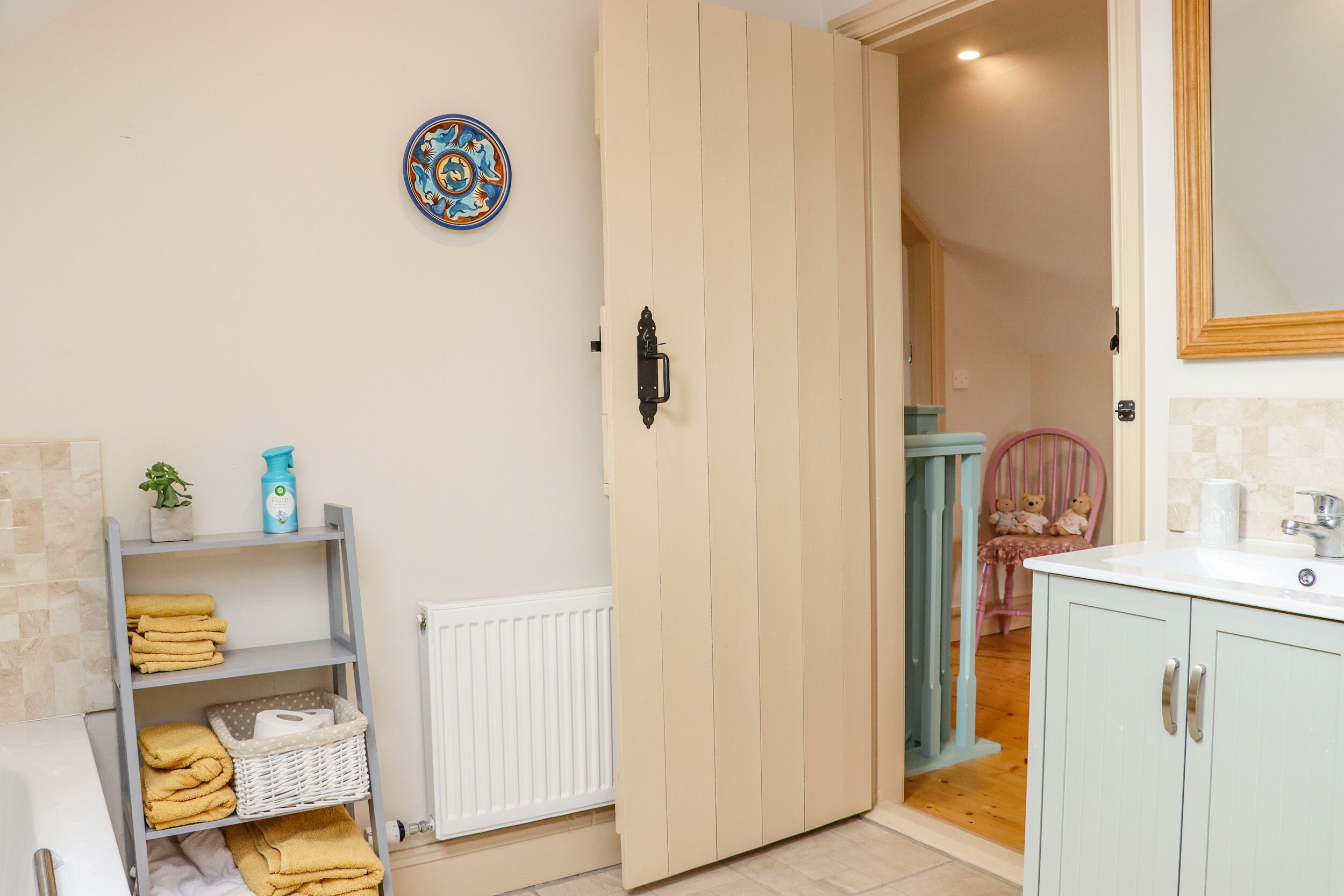 Een badkamer met een houten deur, een plank met handdoeken, een radiator en een spiegel.
