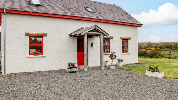 A white building with red trim and a red door, featuring a gravel driveway and potted plants.
