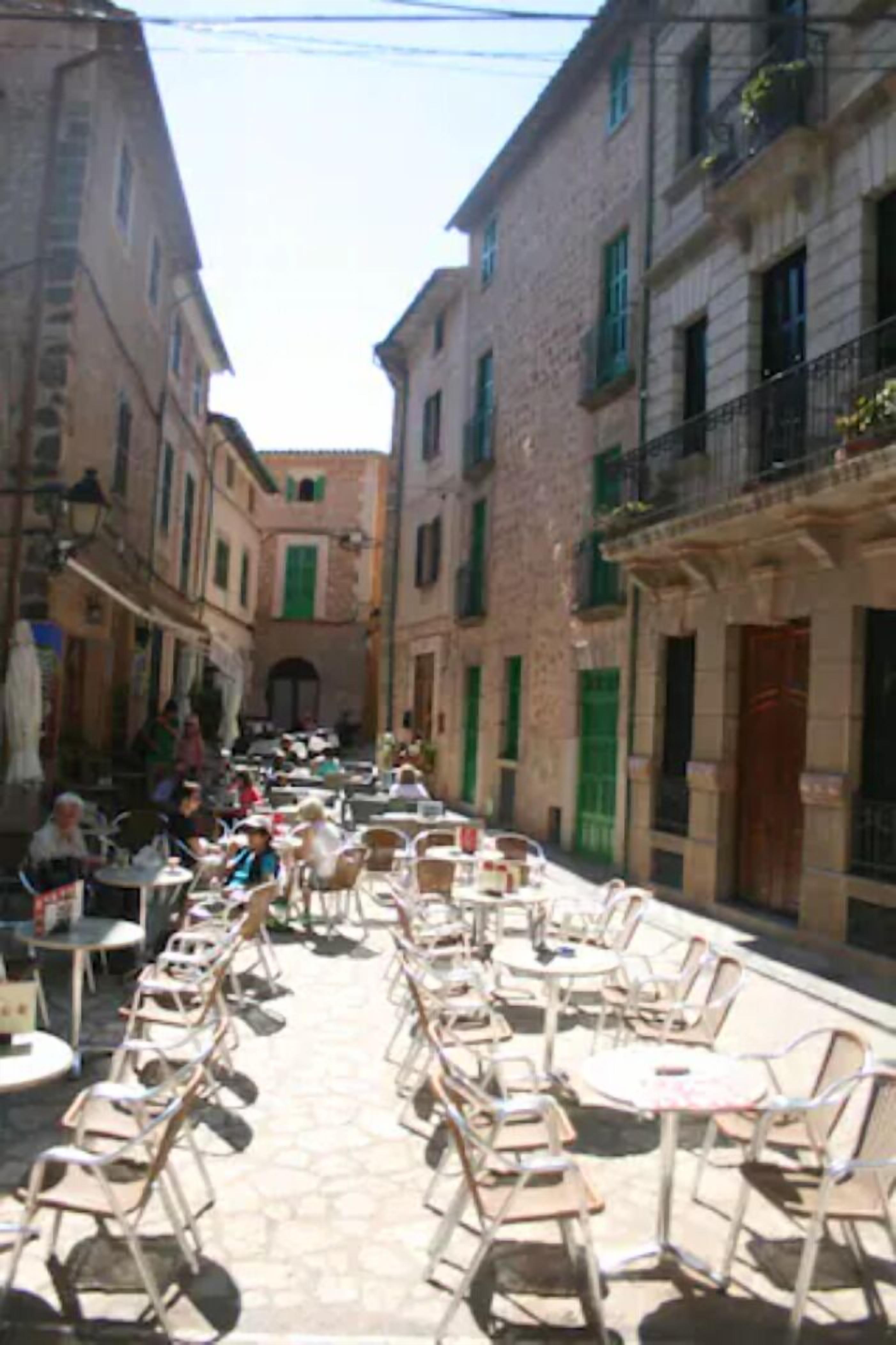 Una calle estrecha con mesas al aire libre y edificios a ambos lados.