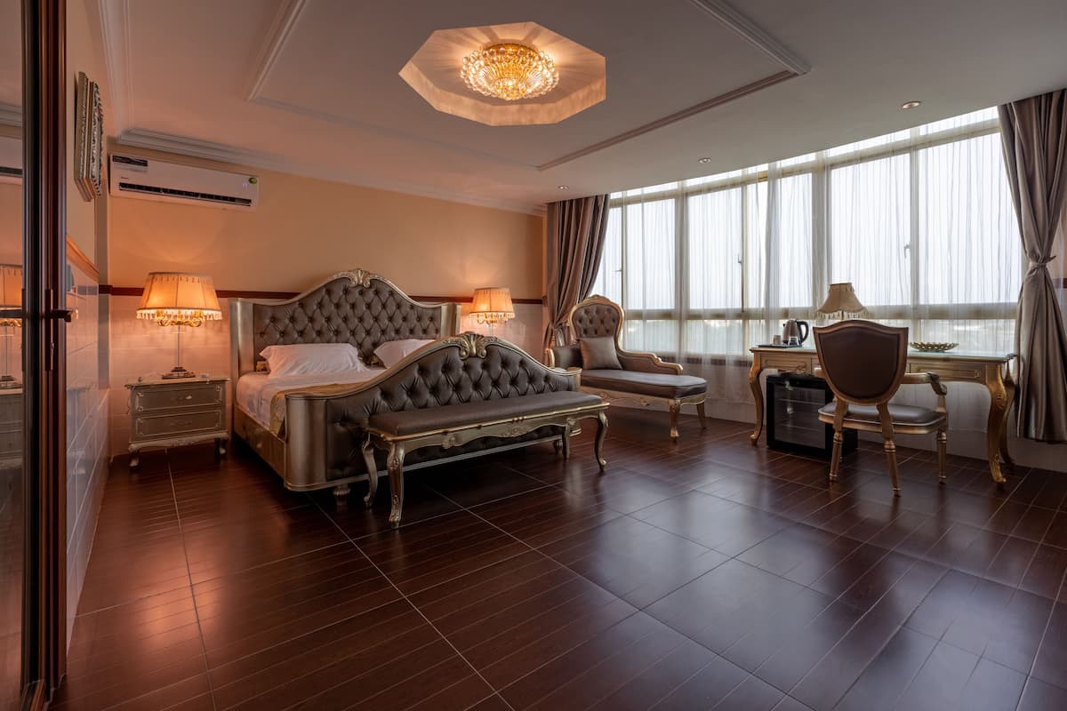 Um quarto luxuoso com uma cama grande, duas mesas de cabeceira, um lustre e vista para a cidade através de amplas janelas.