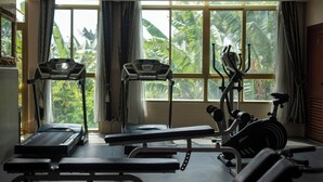 Un gimnasio con equipamiento de ejercicio, una banca y ventanas amplias con vistas a zonas verdes.