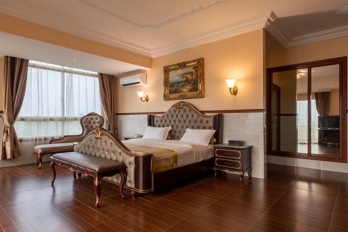 Um quarto espaçoso com uma cama grande, um chaise longue, uma mesa de cabeceira e um espelho.
