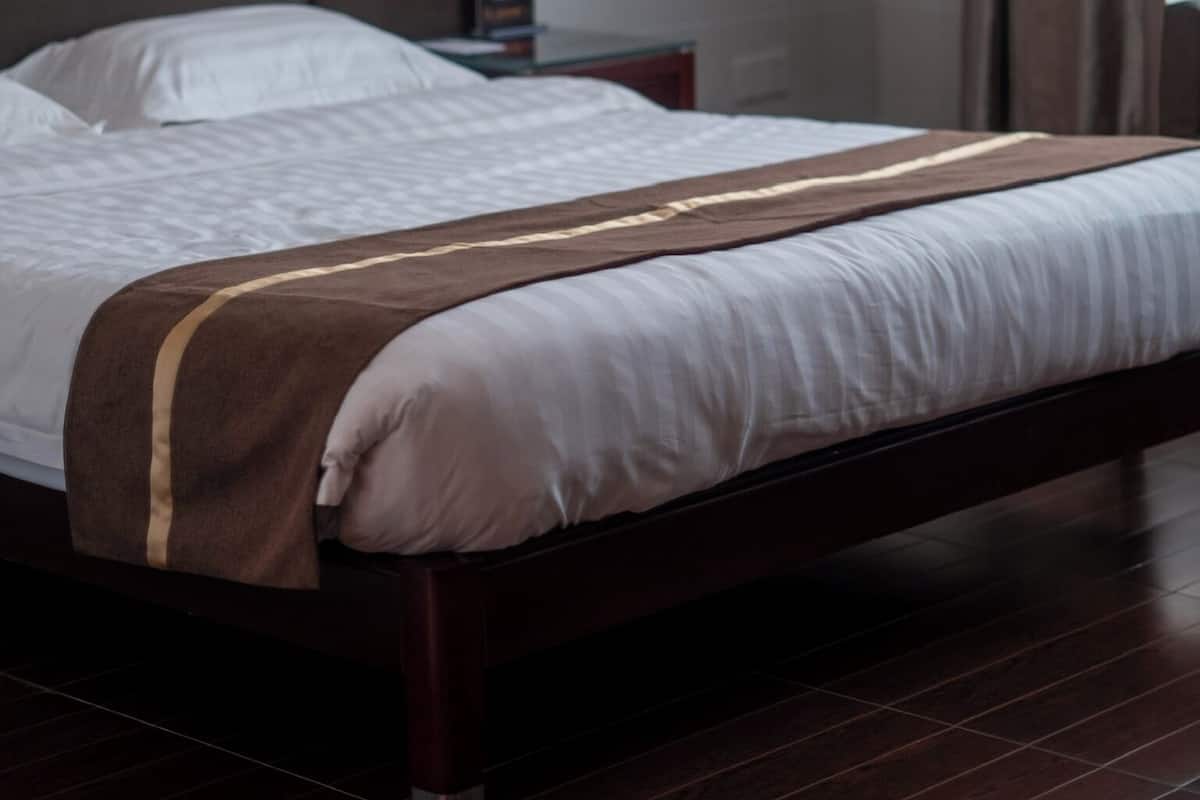 Quarto de hotel com uma cama grande, mesa de cabeceira, relógio e janela com cortinas.