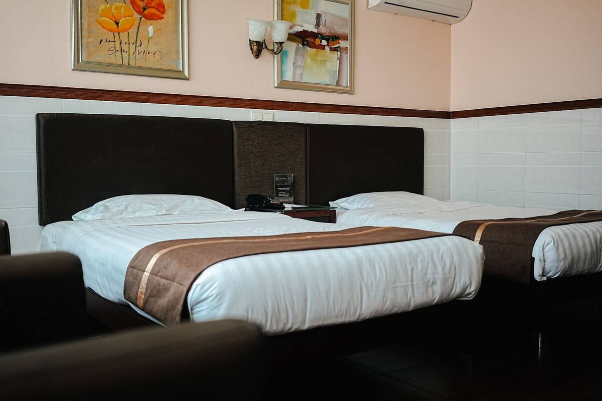 Quarto de hotel com duas camas, mesa de cabeceira, luminária na parede e obras de arte.