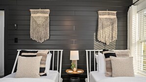 Une chambre avec deux lits, une petite table avec une lampe et des décorations murales en macramé.