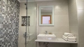 A modern bathroom with a glass shower enclosure, a white sink with a mirror above it, and a tiled shower wall. - Chrysoula’s Convenient Triple Room with Yard (Monemvasia)