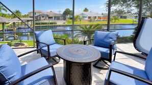 Eine Terrassenfläche mit vier blauen Sitzgelegenheiten und einem runden Tisch, mit Blick auf ein Gewässer und eine Wohngegend.