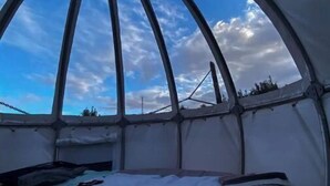 Ein kuppelförmiges Zelt mit einem Bett, einem Fenster und Blick zum Himmel.