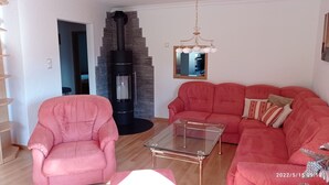 Ein Wohnzimmer mit einem rosafarbenen Sofa, einem Glastisch, einem Steinkamin und einer Holztreppe.