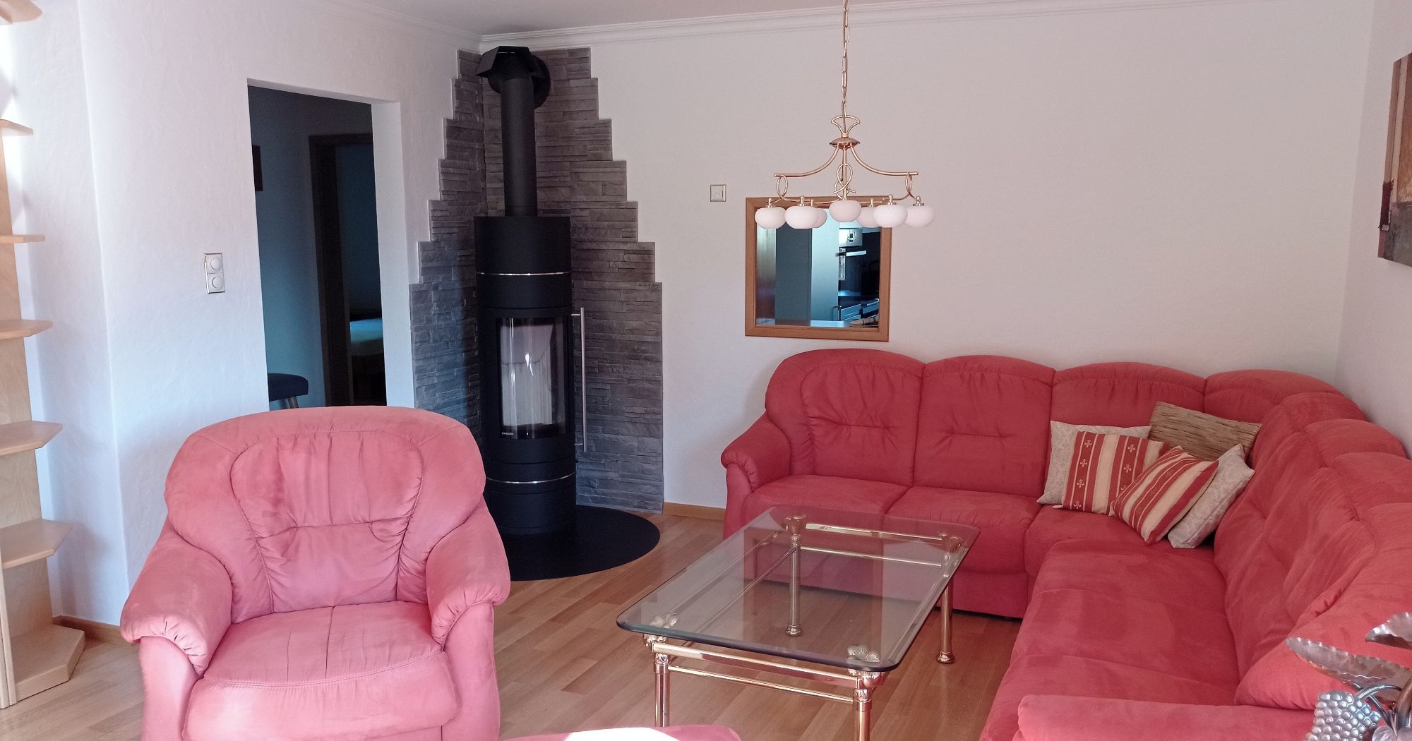 Ein Wohnzimmer mit einem rosafarbenen Sofa, einem Glastisch, einem Steinkamin und einer Holztreppe.