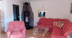 A living room with a pink sofa, a glass coffee table, a stone fireplace, and a wooden staircase. - Vacation apartment (80 m²) with wonderful panoramic view between Schliersee and Tegernsee (Hausham)