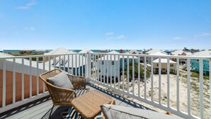 Un balcone con mobili in vimini, vista su case sulla spiaggia e cielo sereno.