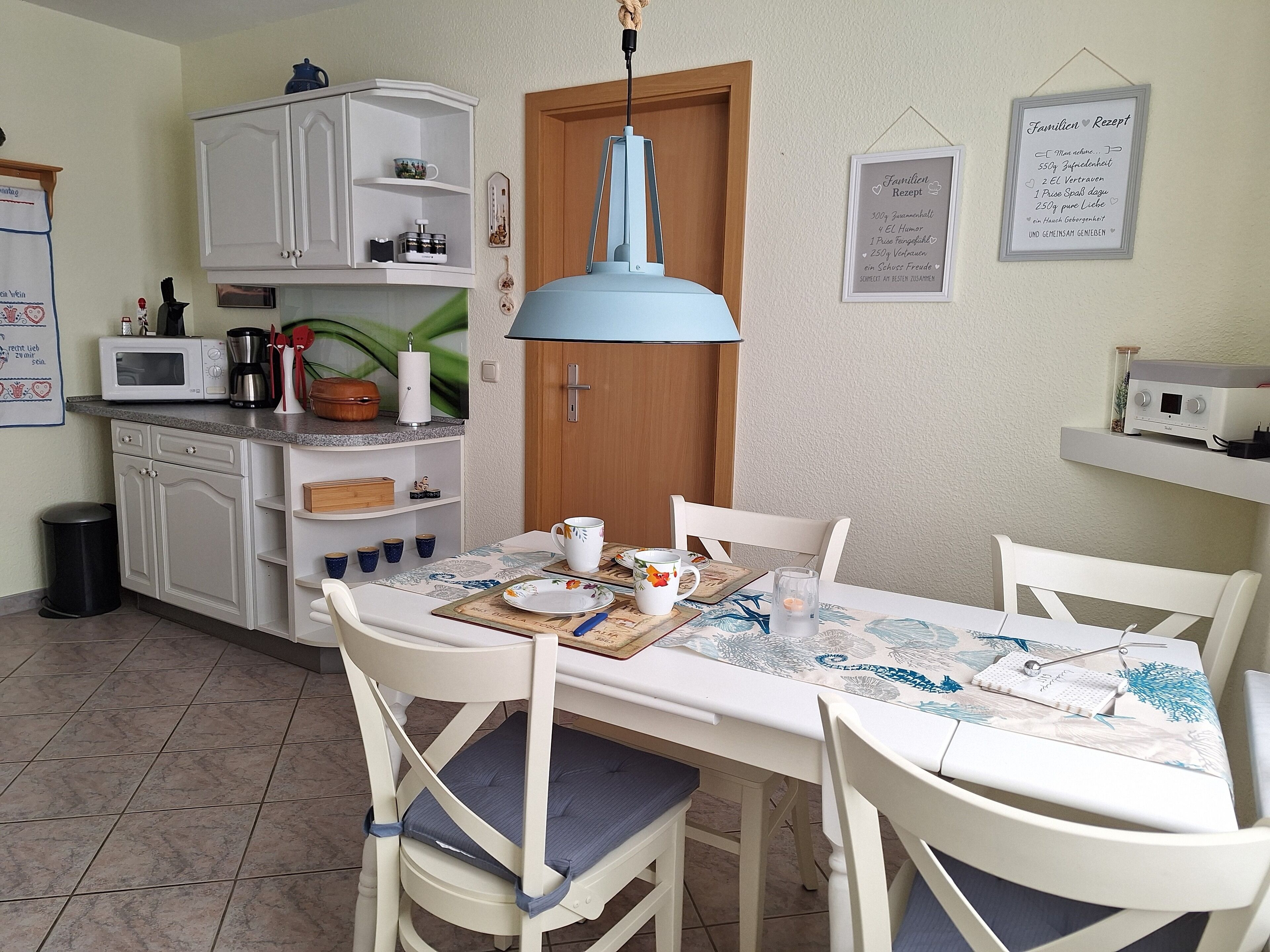 A kitchen with white cabinets, a microwave, and a coffee maker. There is a dining table with chairs and a hanging light fixture.