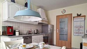 Eine Küche mit weißen Schränken, einem roten Toaster, einem Wasserkocher und einem Kühlschrank. Ein Tisch ist mit einer Unterlage und einer Tasse abgedeckt.