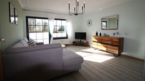 Ein modernes Wohnzimmer mit einer Couch, einem Fernseher, einer Holzkommode und einem großen Fenster.